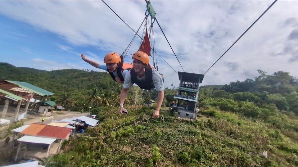 Two people ziplining over lush green landscape in Badian, Cebu.