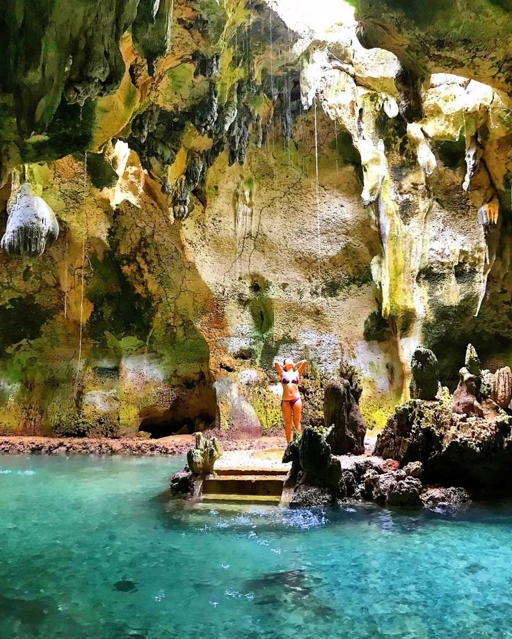 Visitor standing inside Bukilat Cave in Camotes, surrounded by rock formations and turquoise water.