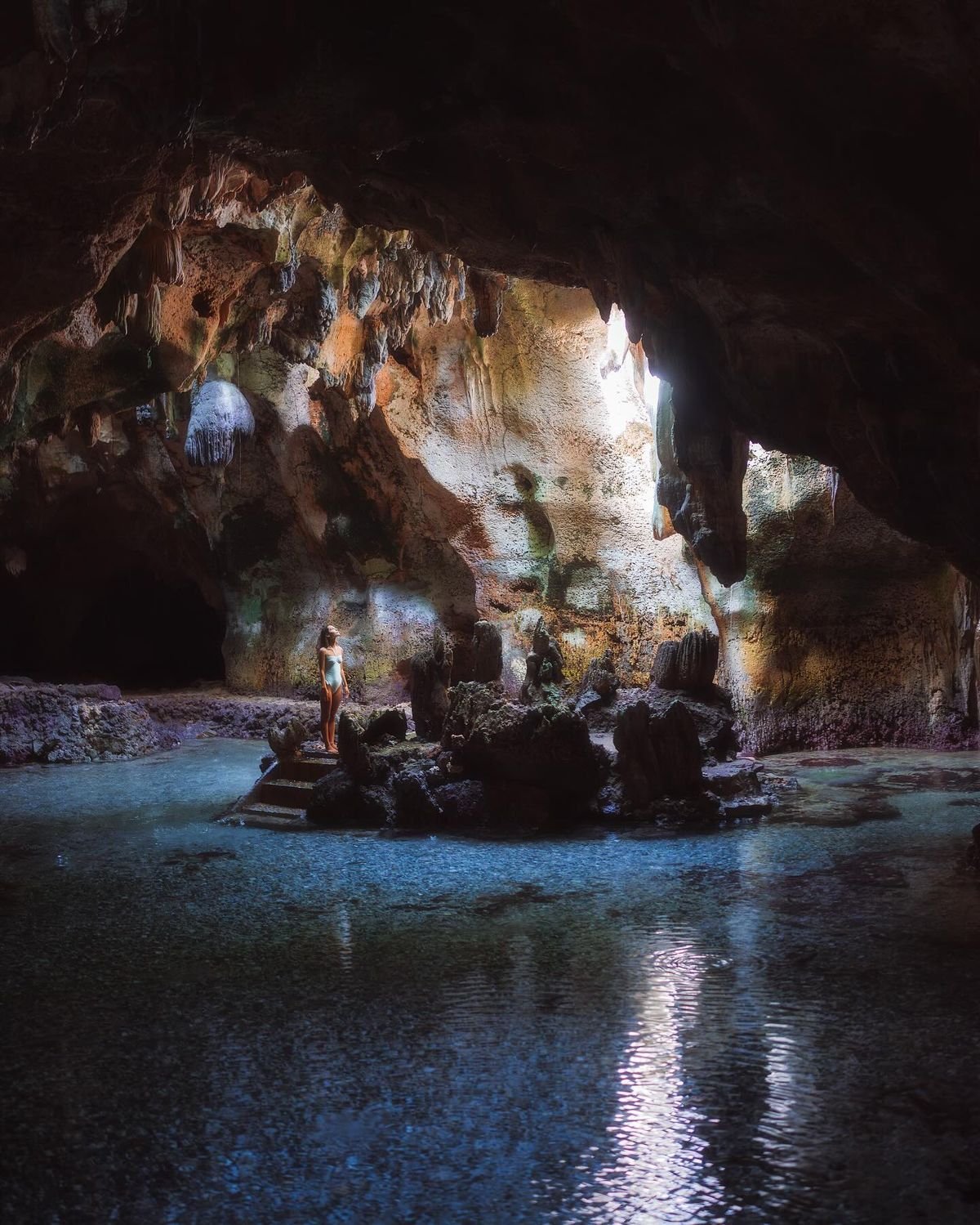 Visitor standing inside Bukilat Cave in Camotes, surrounded by rock formations and turquoise water.